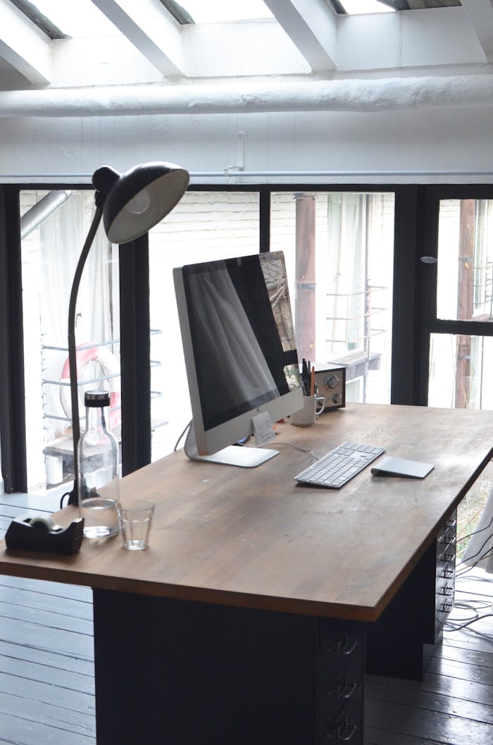 A sleek, minimalist office setup featuring a computer on a wooden desk with natural daylight.
